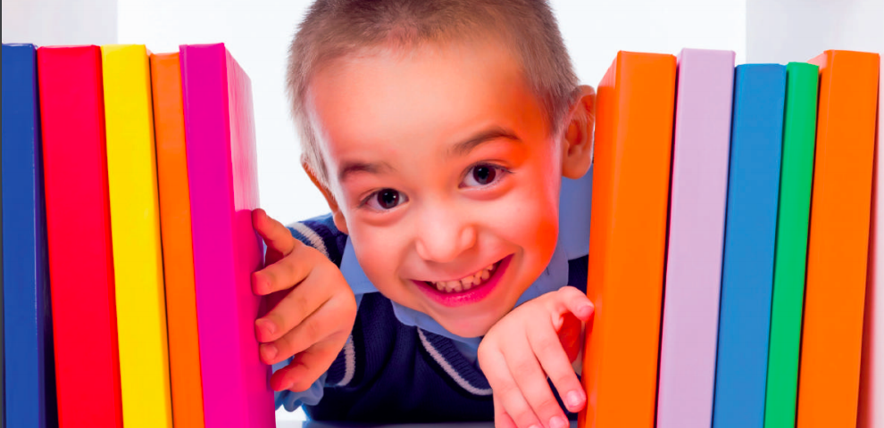 Small school child poking his through a bunch of vibrant coloured library books on a shelf.