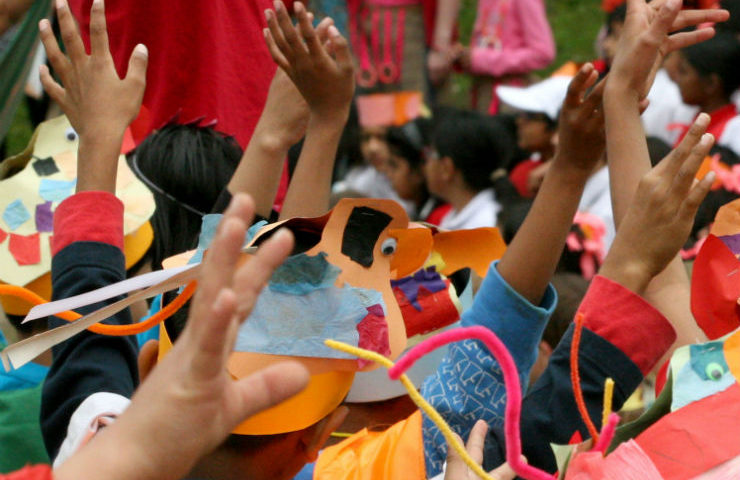 Diverse group of arms in the air, handmade dogs can be seen on the top of children's heads.