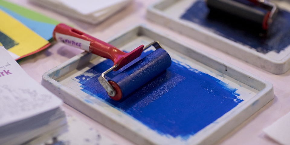 Paint roller on a table - the paint is blue and there are colours across the table.