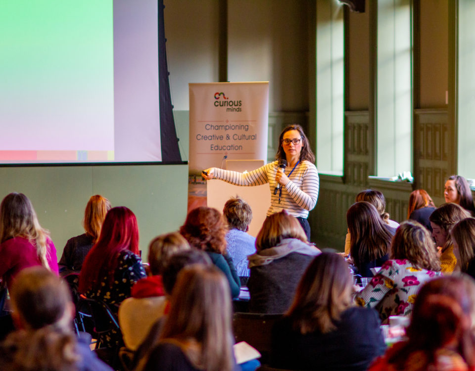 Woman stood in front of a group of people and pointing to a projector screen.