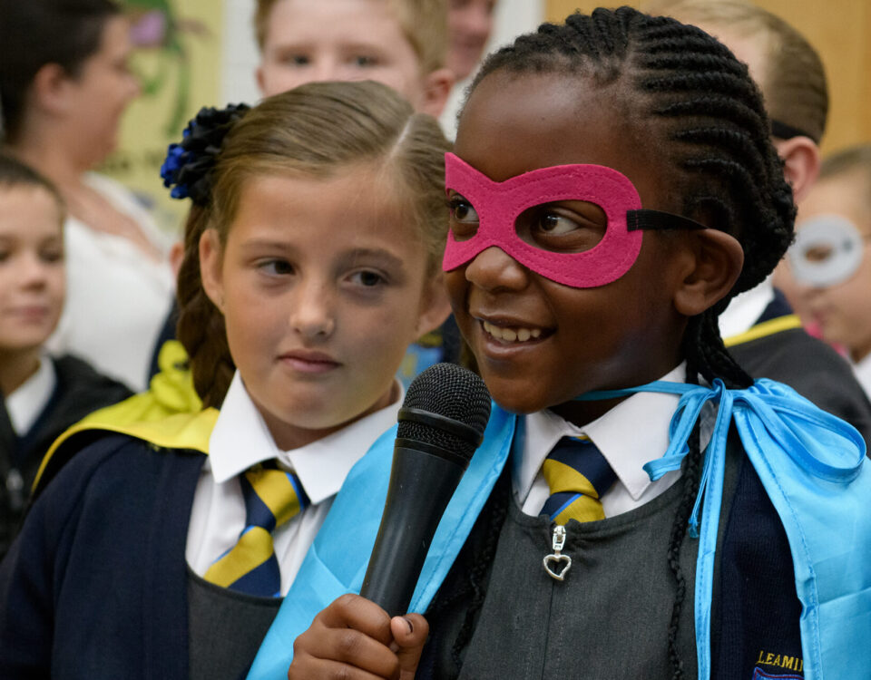 A young school pupil wearing a cape and mask speaks confidently into a microphone - From WoW's Super Heroes project.