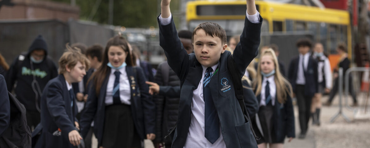 A key stage 3 school pupil on a cultural visit with both thumbs up, surrounded by other children.