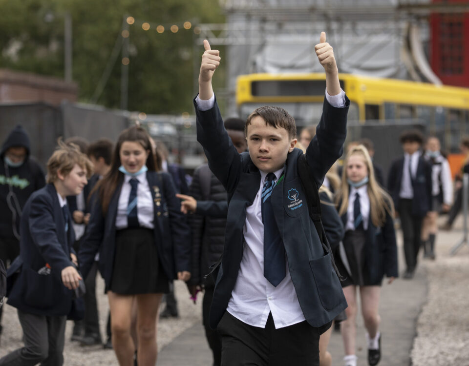 A key stage 3 school pupil on a cultural visit with both thumbs up, surrounded by other children.