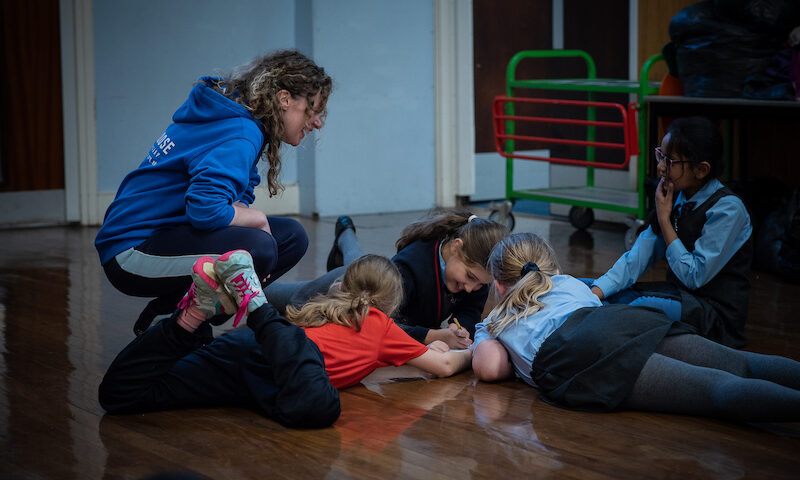 A group of chool children work on the floor with a dance practitioner