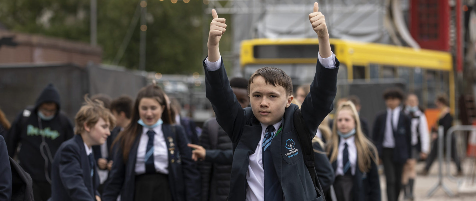 A key stage 3 school pupil on a cultural visit with both thumbs up, surrounded by other children.