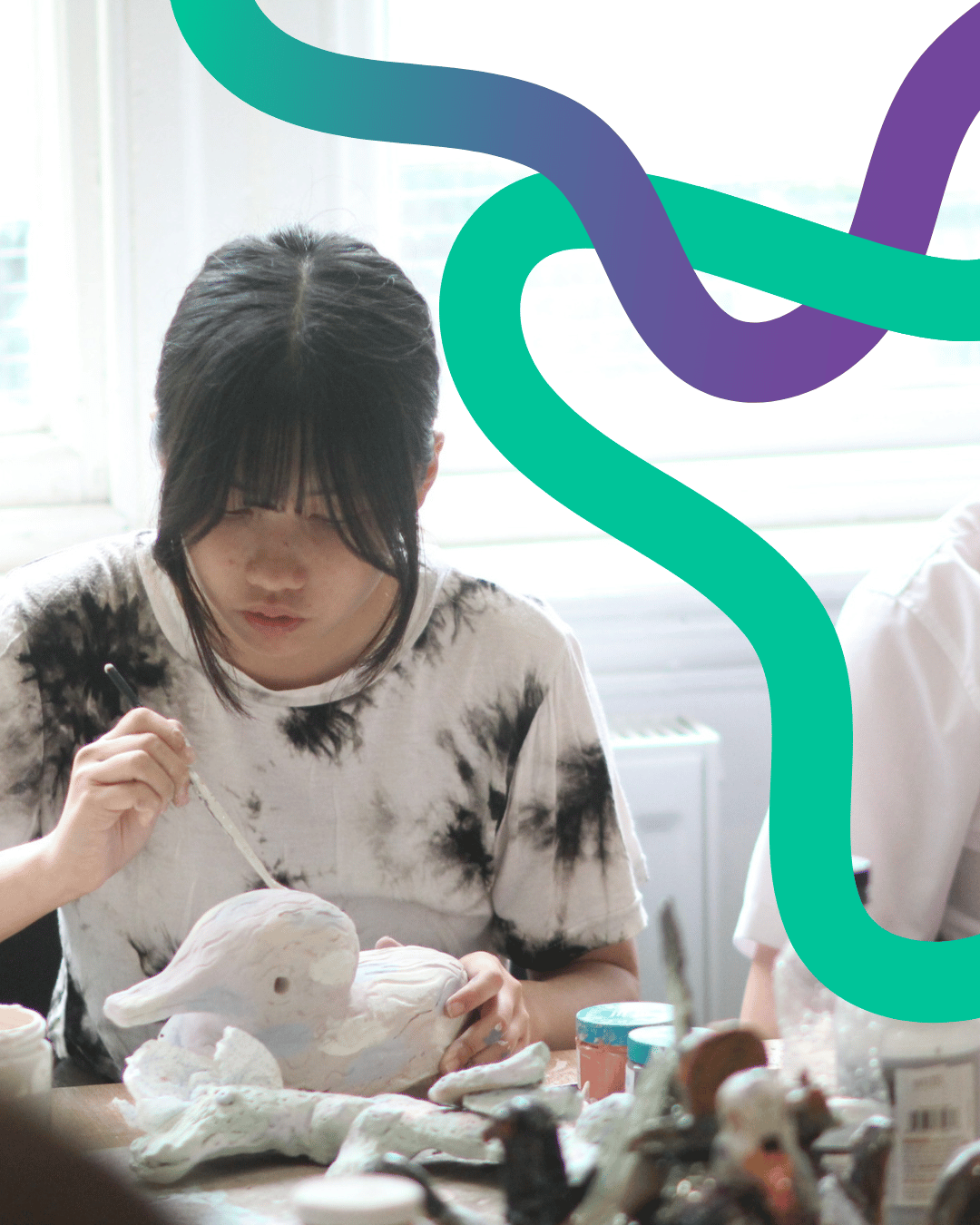 Image shows a young person painting a ceramic duck. She has dark hair tied back in a ponytail and her fringe frames her face. She is concentrating - absorbed in her creation.