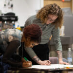 Two young people are working together, stood at a table writing on paper with a felt tip